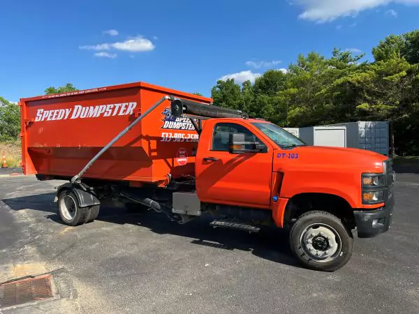 Orange roll‑off truck hauling a dumpster container, illustrating a reliable dumpster rental Columbus service in action.
